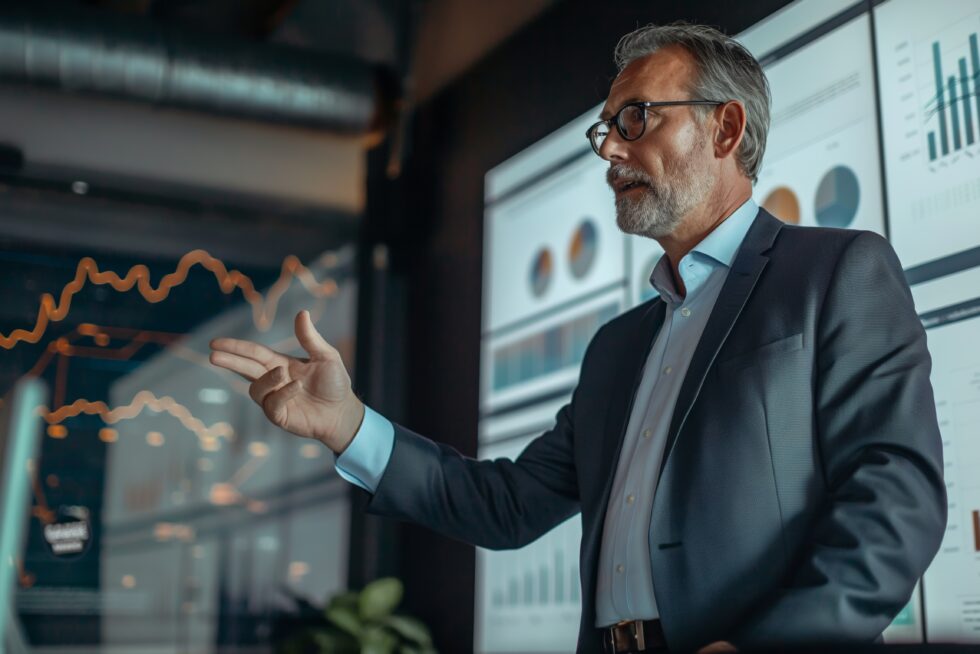 A business professional presenting financial data with charts and graphs displayed on a screen in the background, illustrating growth trends and performance analysis.