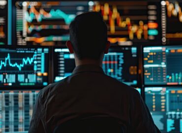 A man is sitting in front of a computer monitor with multiple screens displaying financial data. The man is focused on the screens. Concept of intensity and concentration